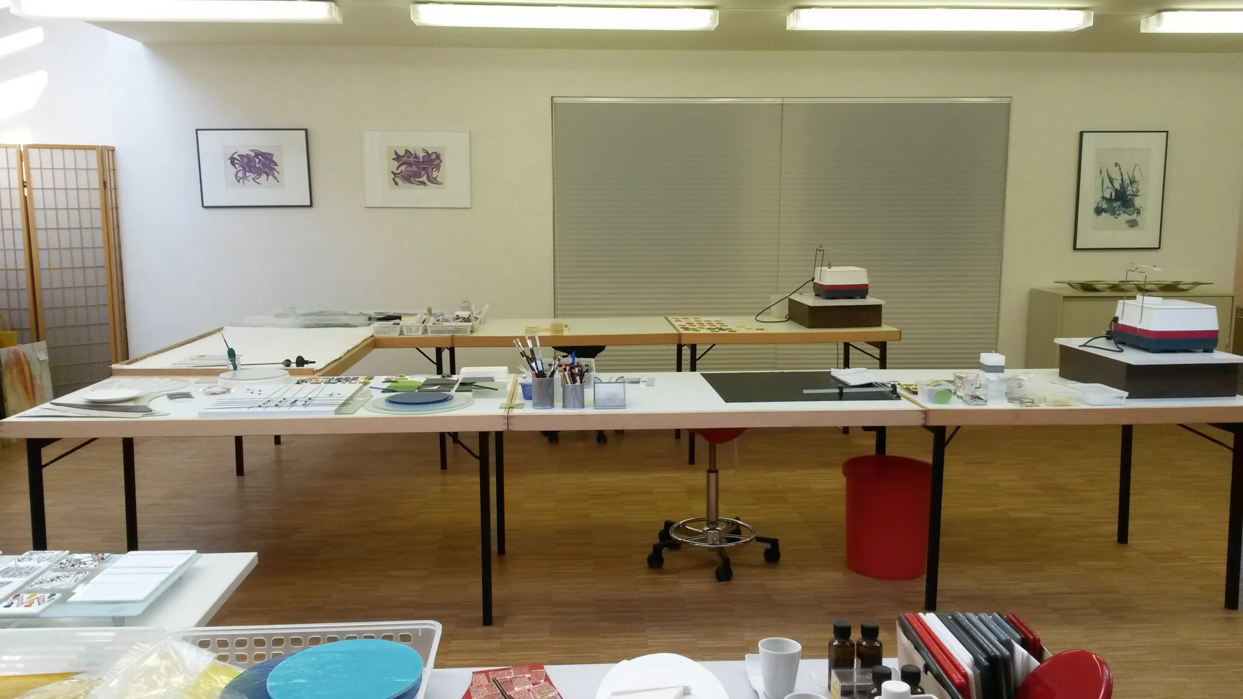 Arbeitstische im Atelier mit Werkzeug, Glasstücken, Schleifmaschinen und Bildern an der Wand